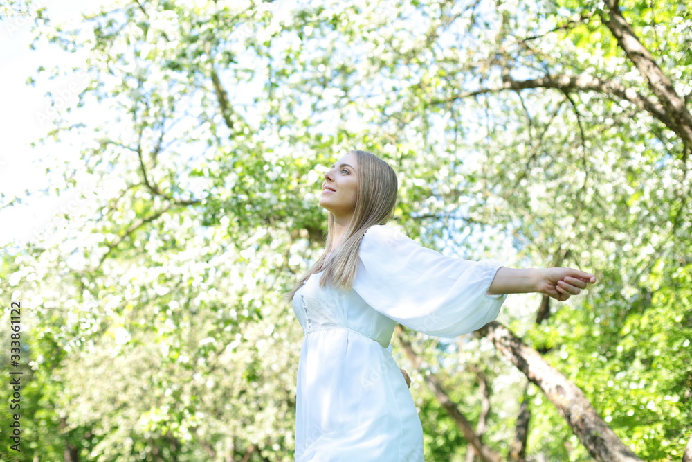 Happy blonde woman on a background of blooming spring garden with her hands raised to the sky
