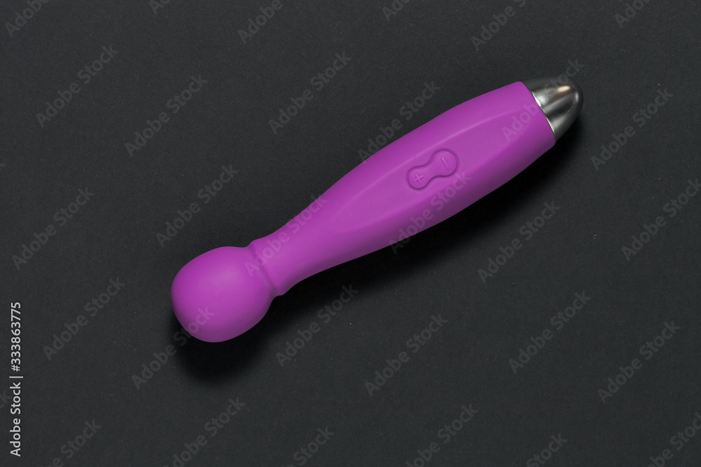 Naklejka premium Erotic pleasure toy on a black background. Sex gadget and masturbation device. A purple rubber and silicone dildo is lying on pink paper. View from above. Place for text. Flat lay. Sex shop concept.