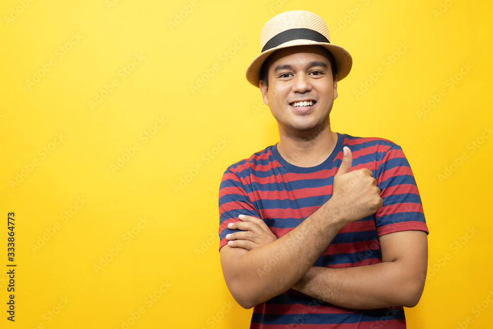 Portrait of cheerful asian man in basic clothing Casual wear red striped T-shirt and wear a hat smiling and show giving thumbs up at camera with showing success. isolated over yellow background. Portrait of cheerful asian man in basic clothing Casual wear red striped T-shirt and wear a hat smiling and show giving thumbs up at camera with showing success. isolated over yellow background.