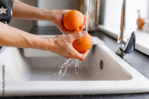 Hands of woman washing ripe orange under faucet in the sink kitchen