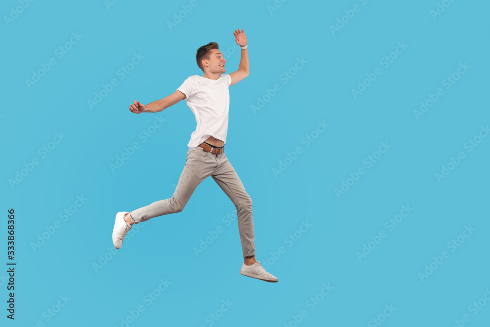 Full length, excited man in casual outfit running quickly, hurrying to his dream, walking in air with enthusiastic face, believing in success and luck. indoor studio shot isolated on blue background
