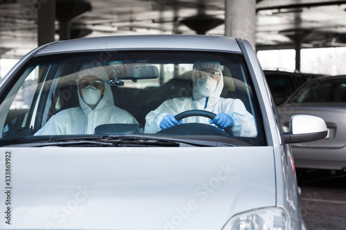Medical worker and virologist in protective suits driving a car