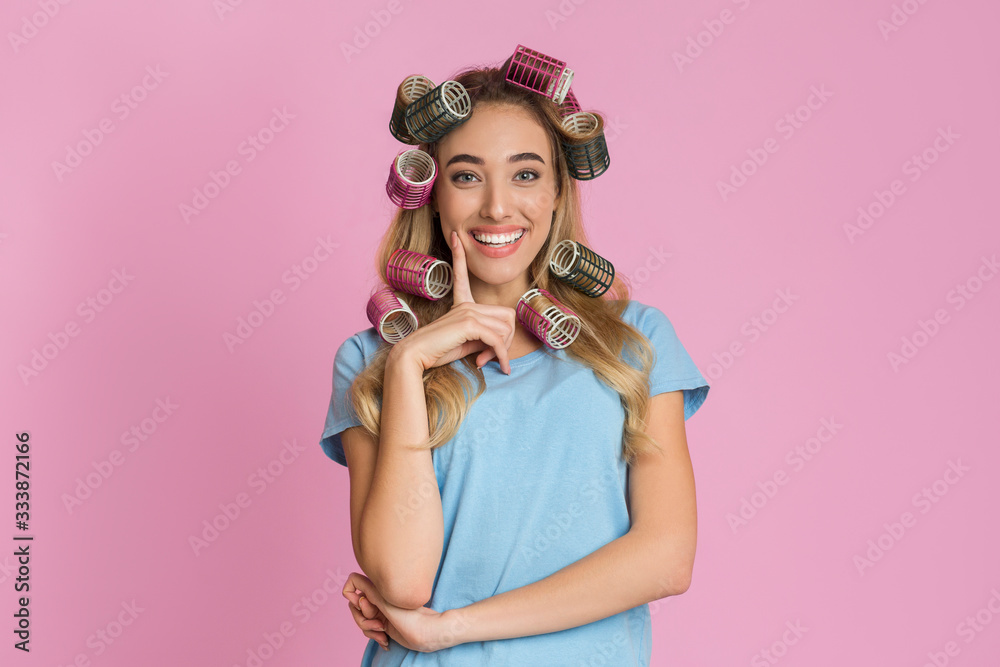Beautiful girl with curlers put finger to her cheek