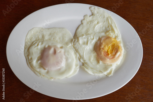Two fried eggs for breakfast on a white plate on a wooden table. 