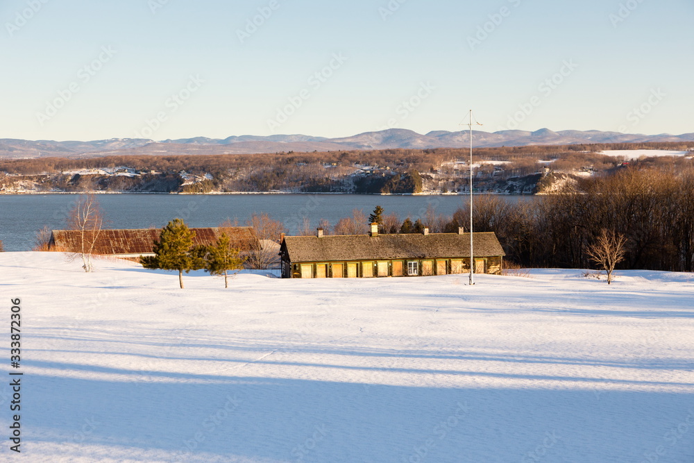 Old shingled roofed long hen house and other farm buildings seen in a snowy field from the Route 132 during a bright early spring morning, Beaumont, Quebec, Canada