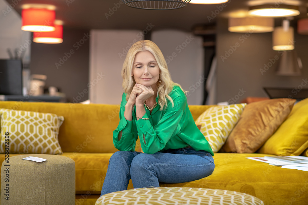 Obraz premium Blonde woman in a green blouse sitting on a yellow sofa