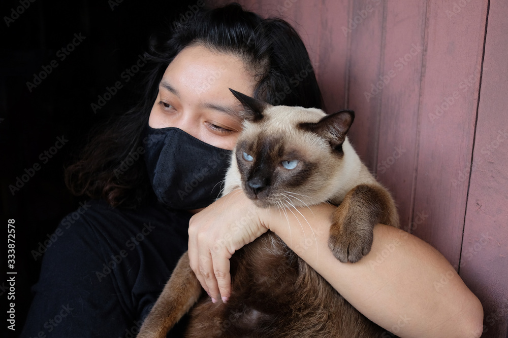 Asian Thai woman carrying a siamese cat and wearing a black cloth mask for prevent the Covid-19 or Corona virus and Epidemic disease at Thailand and around the world. Health and illness concept