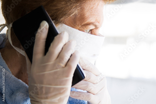 senior woman using mobile phone with mask and disposable medical gloves. Safety measures during the coronavirus outbreak