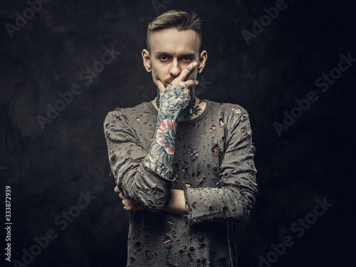 Confident male model posing in a dark studio wearing ripped longsleeve jumper, tattooed in a japanese irezumi style, thinking pose, looking straight into camera photo