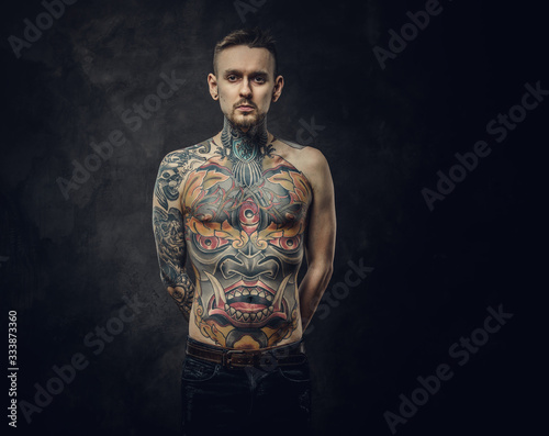 Assertive tattoo artist posing in a dark studio with a half-naked body wearing jeans, tattooed in a japanese irezumi style, looking cool and confident. photo