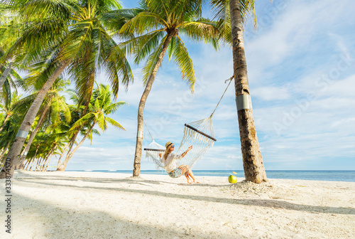 Woman in hat sitting in hammock on the beach. Travel and vacation concept.