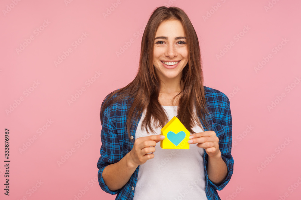 I love my new home. Portrait of charming smiling girl in checkered shirt pleased with property purchase, holding paper house with heart inside. indoor studio shot isolated on a pink background. I love my new home. Portrait of charming smiling girl in checkered shirt pleased with property purchase, holding paper house with heart inside. indoor studio shot isolated on a pink background.