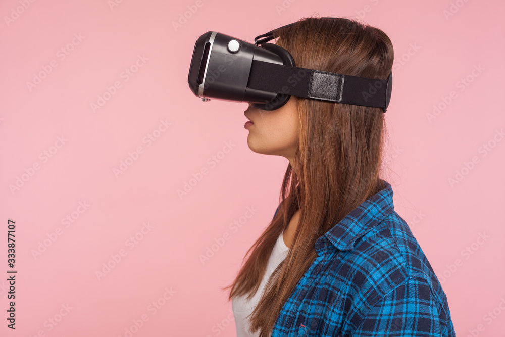 Closeup side view of serious gamer girl in checkered shirt wearing vr headset, playing virtual reality game, copy space for technology advertisement. indoor studio shot isolated on pink background Closeup side view of serious gamer girl in checkered shirt wearing vr headset, playing virtual reality game, copy space for technology advertisement. indoor studio shot isolated on pink background