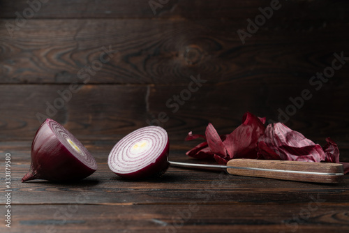 Sliced ​​red onion, onion peel and knife on a brown wooden background