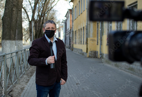 A middle- aged European journalist in a protective medical mask is reporting in a deserted city.