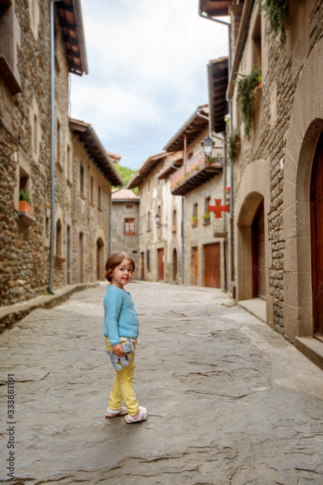 Adorable toddler girl walking in a small ancient medieval village Rupit, in the territory of the Natural Park of the volcanic Garrotxa. Family summer vacation. Catalonia, Spain