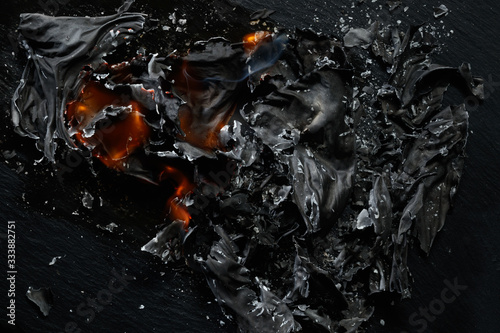Burning piece of black paper on a black background.