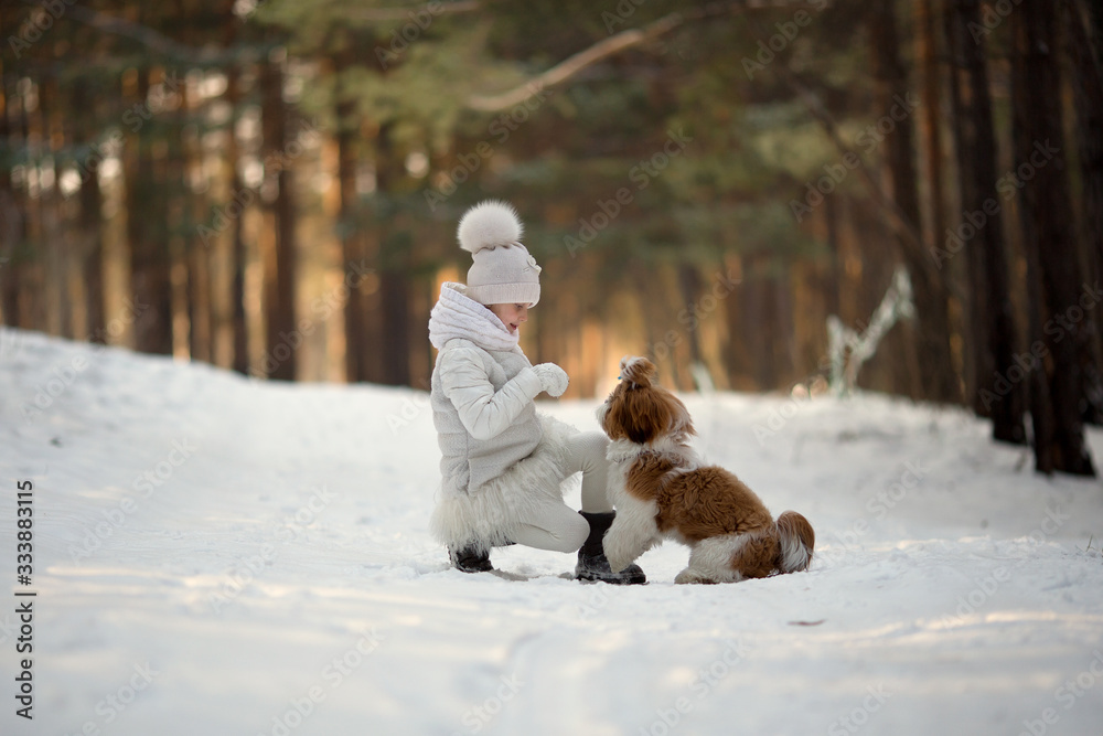 Cute little girl in a white coat with a dog walk in the winter forest. A child is training a dog. Obedience training. Children and animals. Faithful friends of man.
