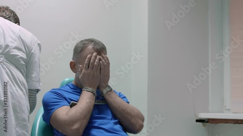 Man sits in chair waiting for doctor to start a procedure. He stuffs his head with hands in despair. Brain examination. photo