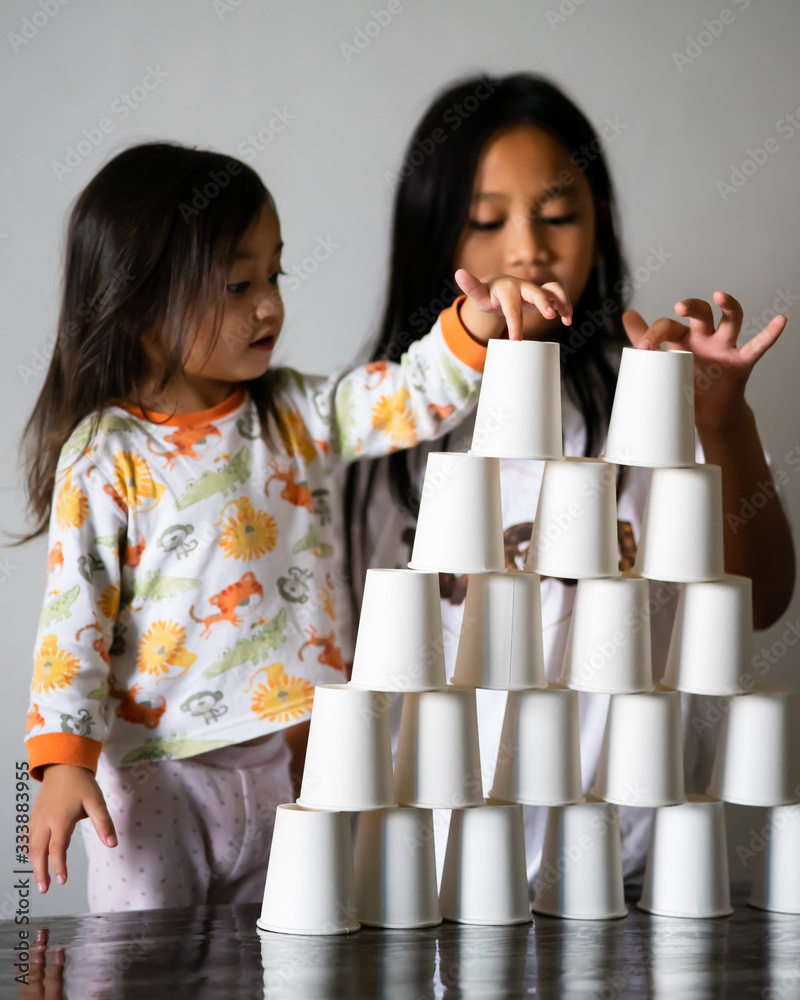 Kids Playing with white paper cups building a cup tower on the table ...