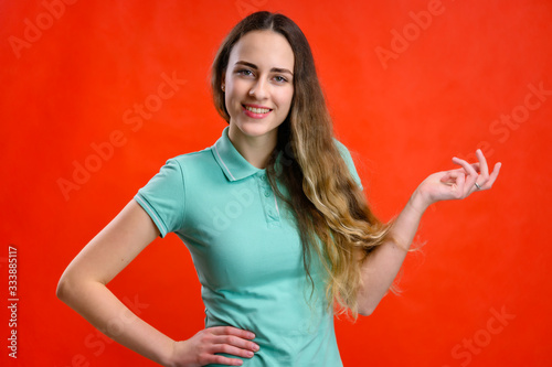 Portrait of a young beautiful girl on a red background. A model with long hair is talking to the camera, showing hands.