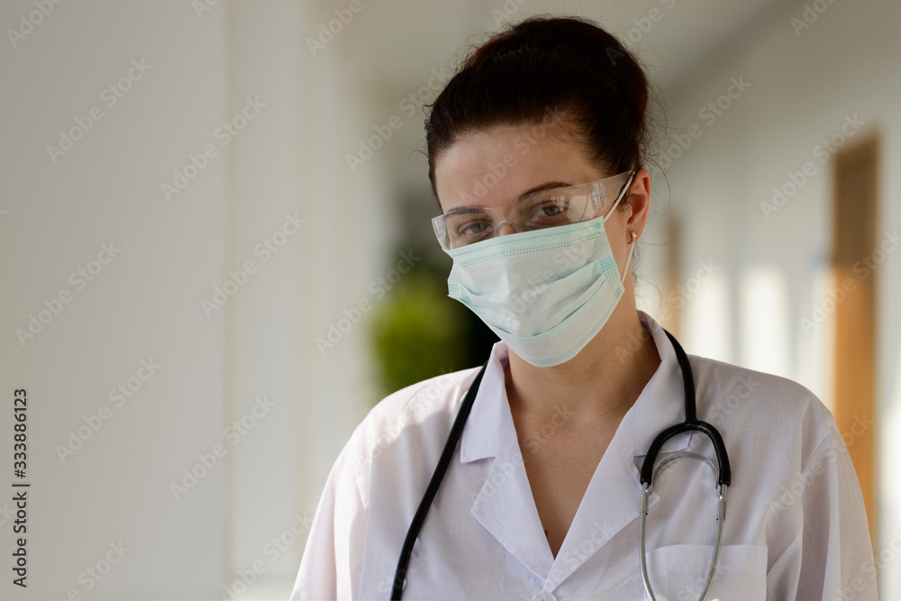 Female doctor scientist in lab coat, defensive eyewear and mask standing indoors. Nurse in white medical uniform. Female doctor scientist in lab coat, defensive eyewear and mask standing indoors. Nurse in white medical uniform.