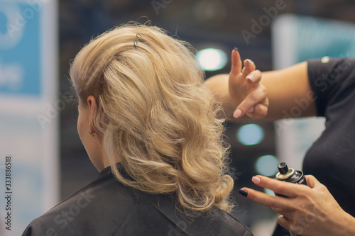 Closeup of hairdresser hands using hairspray styling on woman's healthy golden hair at barber salon