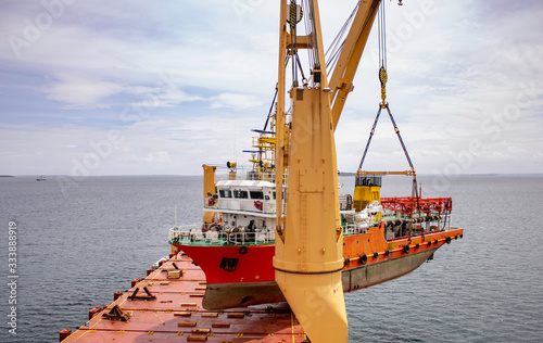 a scientific ship is loaded onto a deck of a heavy lift vessel  by tandem of two cranes with a pontoon installed