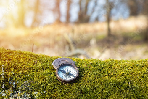  Vintage compass navigation device on the moss in the forest with soft sunlight. Copy space. Travel, camping concept.