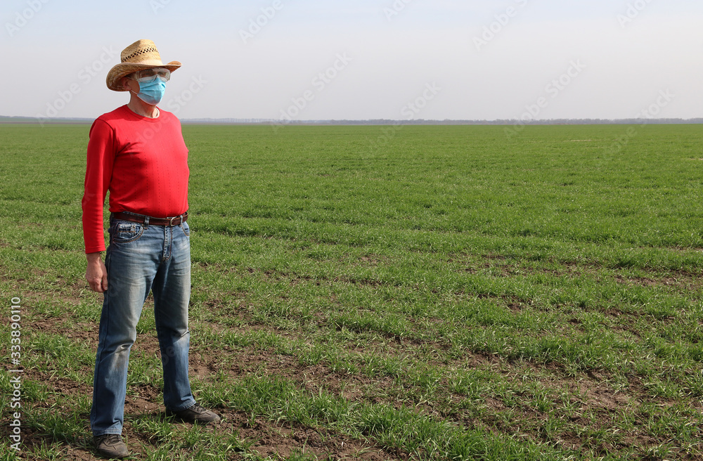 Farmer wearing the protective medical mask and safety goggles at his wheat field. Coronavirus protection.