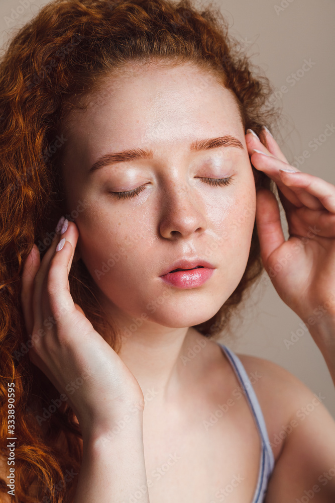 a beautiful red-haired girl washed her face and closed her eyes. Teenage skin care concept. Shot in a studio on a beige background, without makeup, closeup a beautiful red-haired girl washed her face and closed her eyes. Teenage skin care concept. Shot in a studio on a beige background, without makeup, closeup