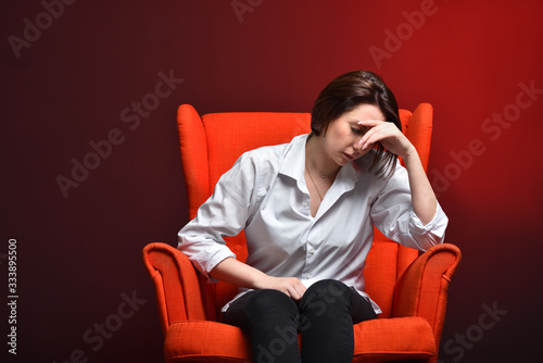 A stressed woman holds her head while sitting in a red chair during a coronavirus pandemic. The concept of viral danger, stress and fear © pridannikov