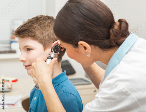 Audiologist examining boy ear , using otoscope, in doctors office. Child receiving a hearing test