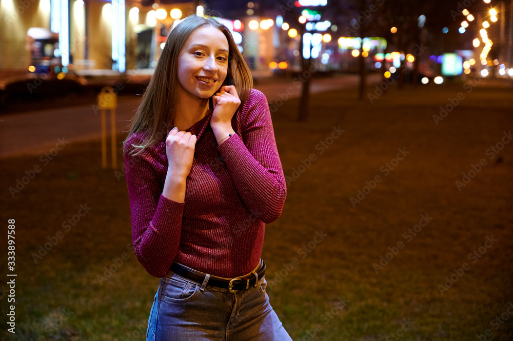 Photo of a cute teen girl one night in the light of the city lights of an outdoor building.