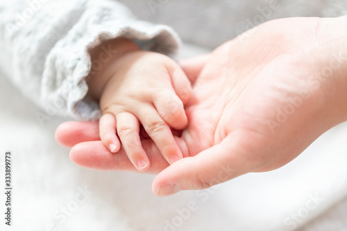 明るい部屋の中で赤ちゃんの手を握る母親の手