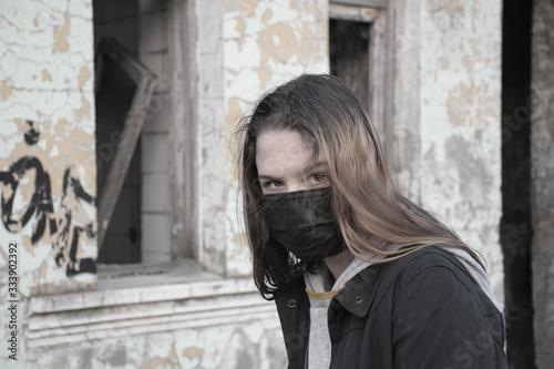 Teenager girl in a black medical mask, on the background of an abandoned post-apocalyptic building. Consequences of COVID-19 Coronavirus protection. After a pandemic