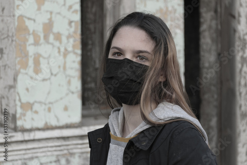 Teenager girl in a black medical mask, on the background of an abandoned post-apocalyptic building. Consequences of COVID-19 Coronavirus protection. After a pandemic