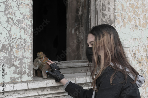Teenager girl in a black medical mask with an old plush toy on the background of an abandoned and destroyed building. Consequences of COVID-19 Coronavirus protection. After a pandemic
