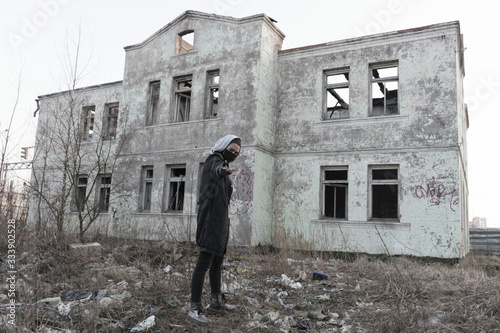 Teenager girl in a black medical mask on the background of an abandoned and destroyed building. Consequences of COVID-19 Coronavirus protection. After a pandemic