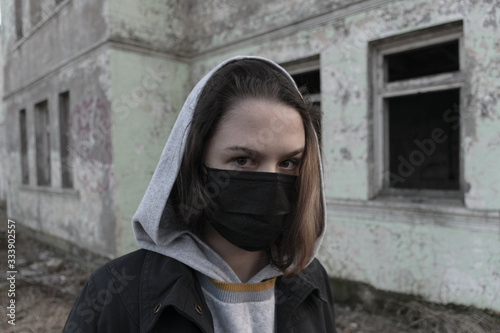 Teen Girl in a medical mask, looking at the camera on the background of an abandoned building. Consequences of COVID-19 Protection against coronavirus. After a pandemic