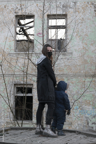 A girl in a black medical mask, with a small child on the background of an abandoned post-apocalyptic building. Consequences of COVID-19 Coronavirus protection. After a pandemic