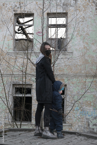 A girl in a black medical mask, with a small child on the background of an abandoned post-apocalyptic building. Consequences of COVID-19 Coronavirus protection. After a pandemic