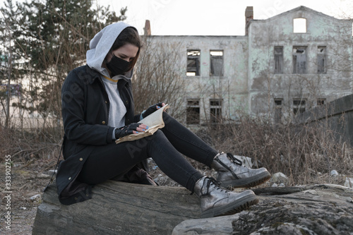 Girl in a black medical mask, Reads a book on the background of an abandoned post apocalyptic building. Consequences of COVID-19 Coronavirus protection. Portrait of a teenage girl. After a pandemic
