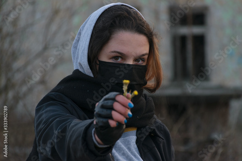 Teen Girl in a medical mask, with flowers on the background of an abandoned building. Consequences of COVID-19 Protection against coronavirus. After a pandemic.