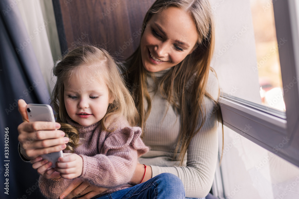 Beautiful woman and her cute little daughter are doing selfie using a smart phone. Beautiful woman and her cute little daughter are doing selfie using a smart phone.