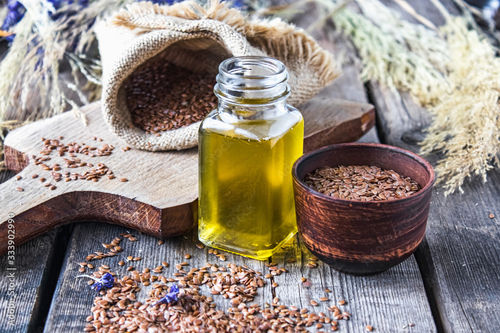 Flaxseed oil in a jar next to flax seeds on a background of old boards. Flaxseed oil in a jar next to flax seeds on a background of old boards.