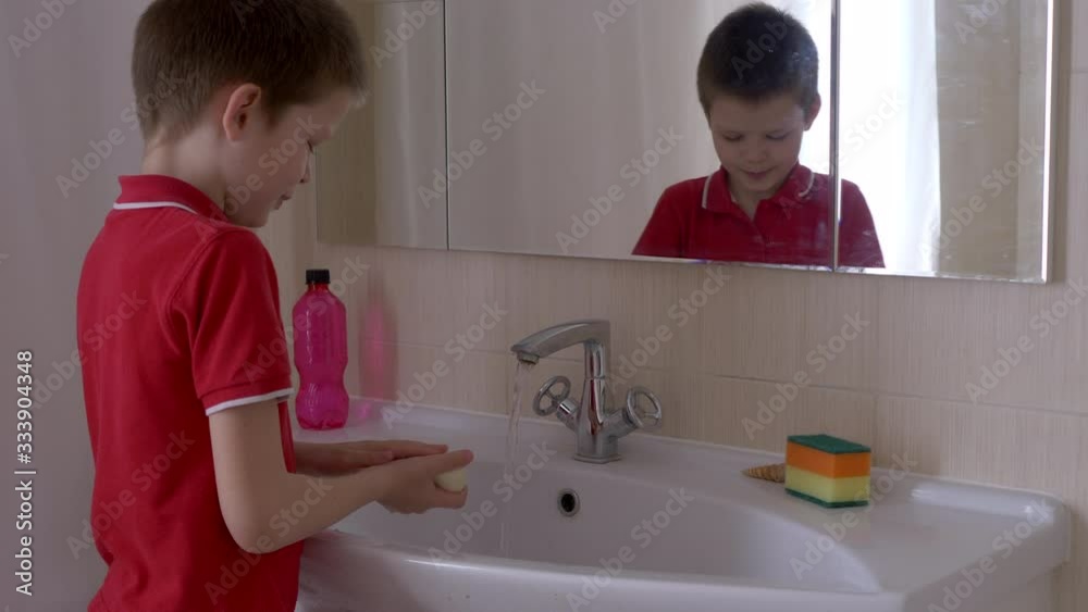 Happy blond boy washes his hands with soap. Child playing with soap and water in sunny bathroom with window. Water activities for children. Hygiene and skin care for pupil. antivirus prevention Happy blond boy washes his hands with soap. Child playing with soap and water in sunny bathroom with window. Water activities for children. Hygiene and skin care for pupil. antivirus prevention
