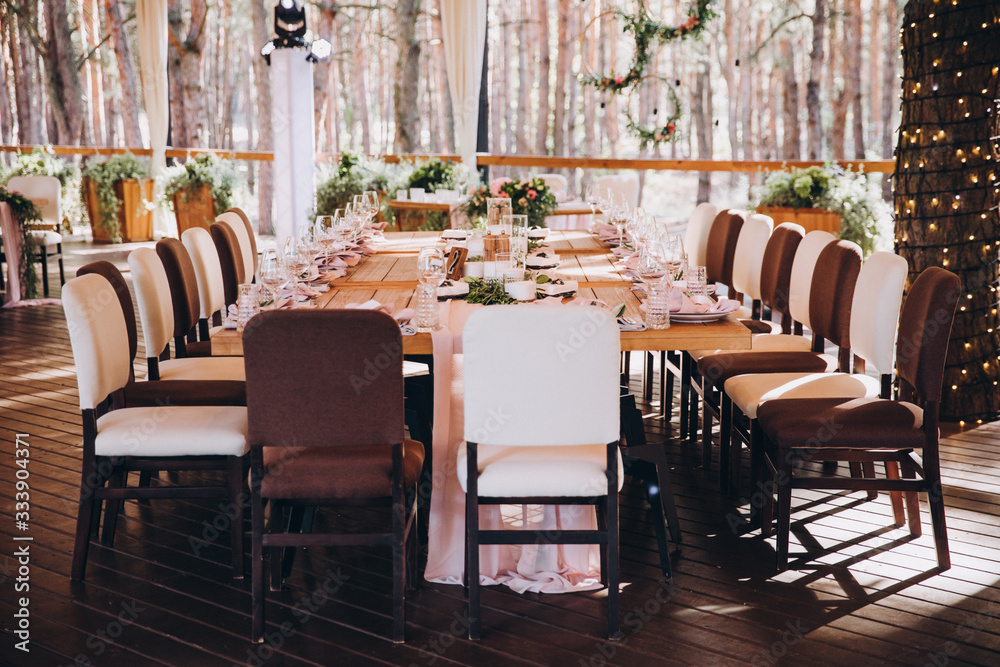 wooden banquet tables decorated with floral arrangements, on the tables are plates, glasses and candles