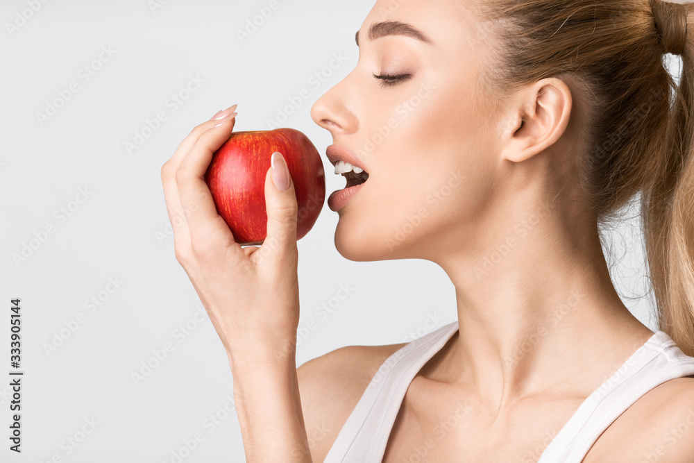 Girl Biting Red Apple Posing On Gray Background, Studio Shot Girl Biting Red Apple Posing On Gray Background, Studio Shot