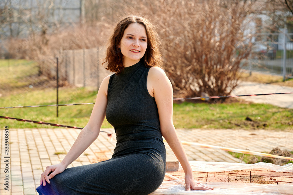 Portrait of a beautiful slender brunette girl sitting outdoors in the spring sun in the city